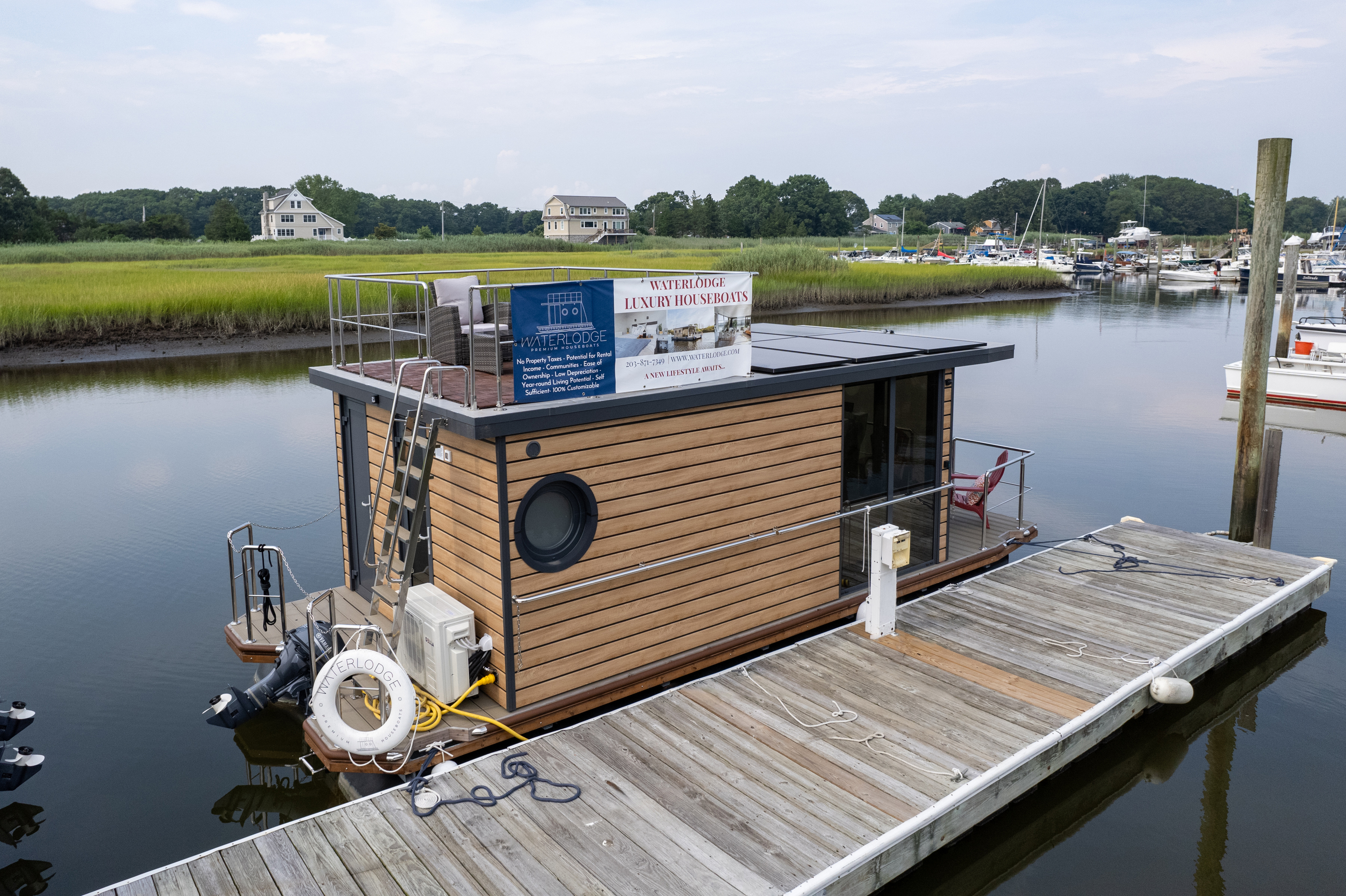 A modern floating house on a lush green marshland with round windows, a flat roof, and a lifebuoy.