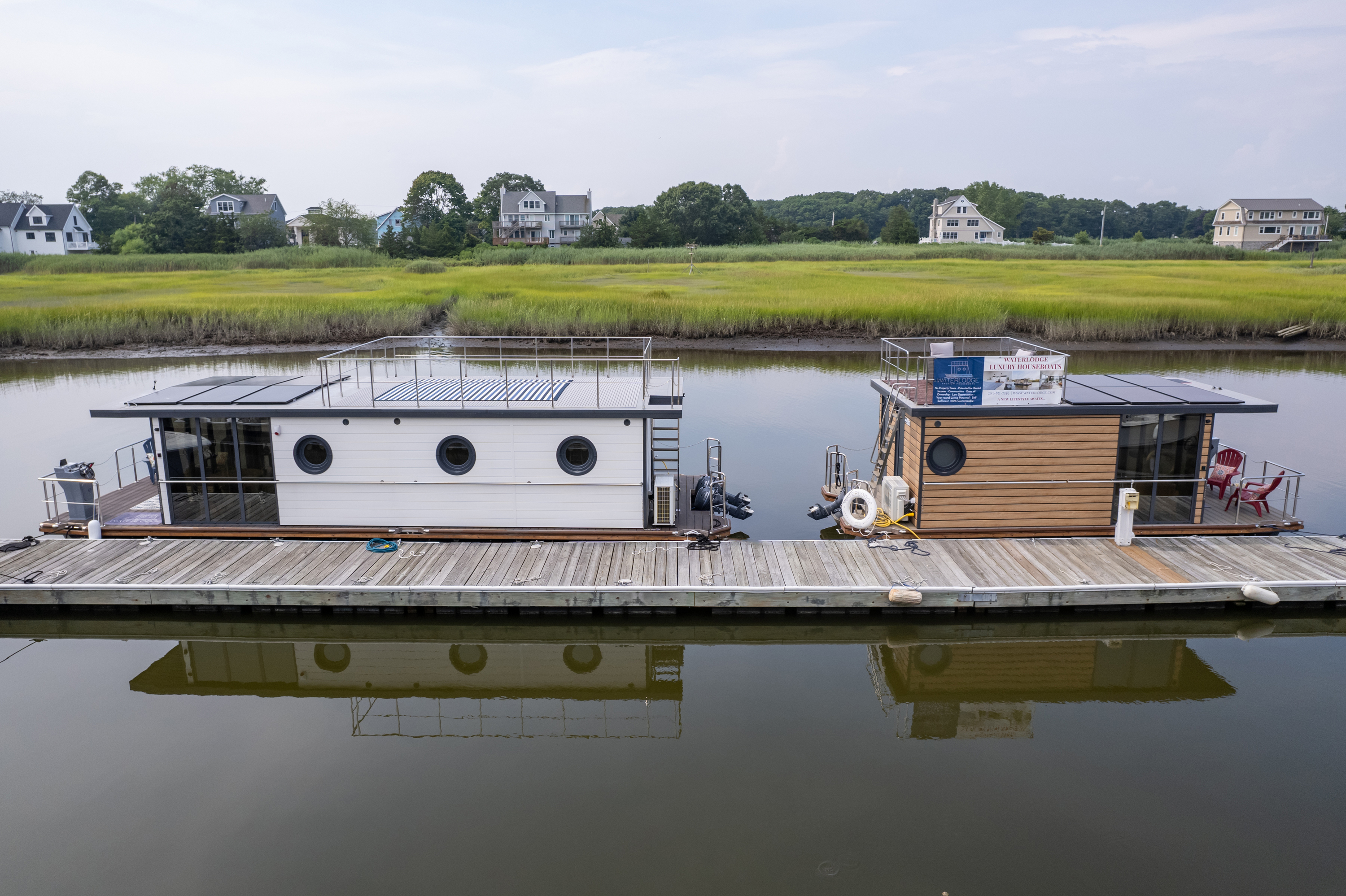 A unique houseboat with round windows docked on a calm river, surrounded by greenery.