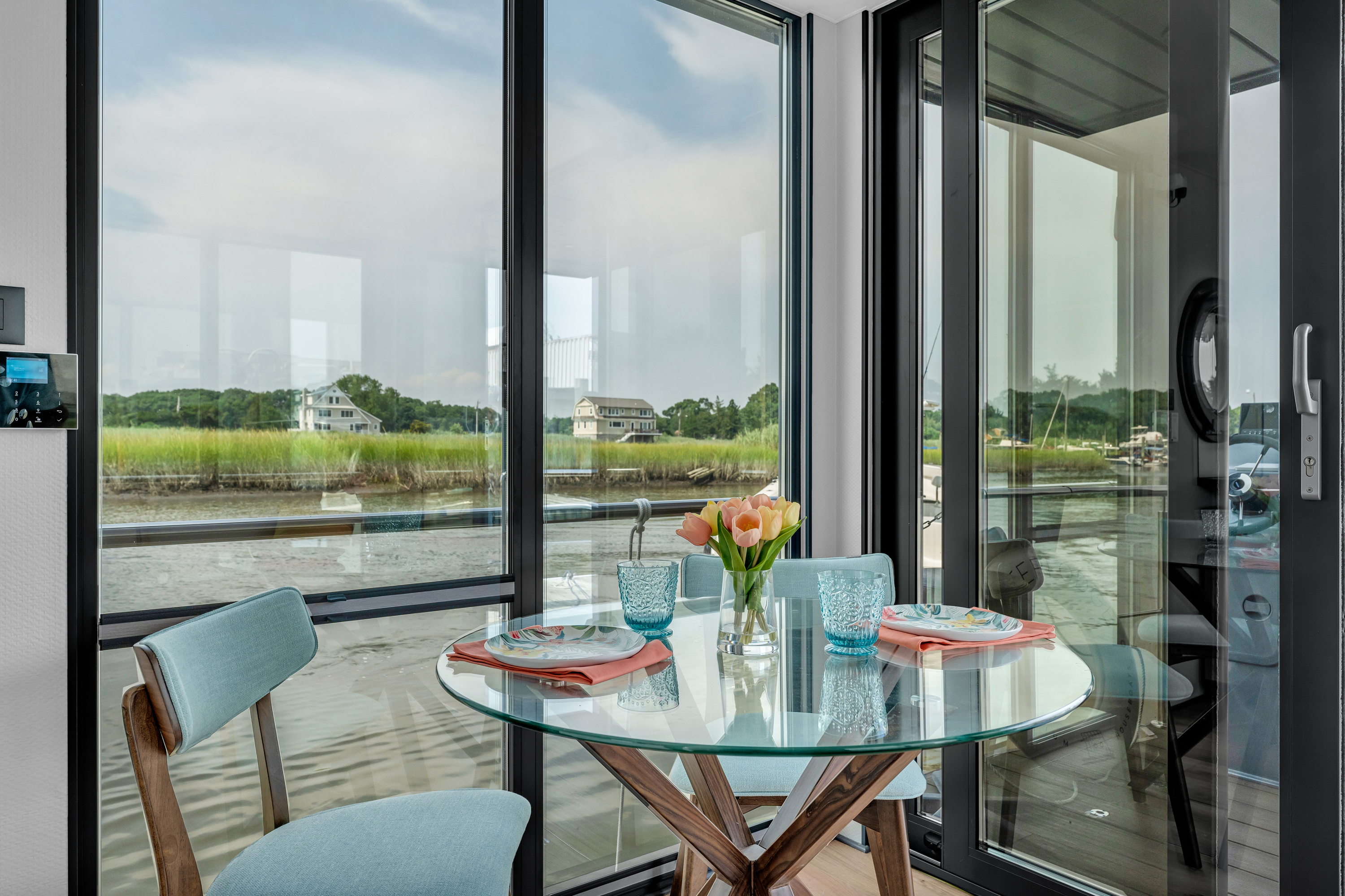 A glass table with flowers, overlooking a marsh from a modern home.