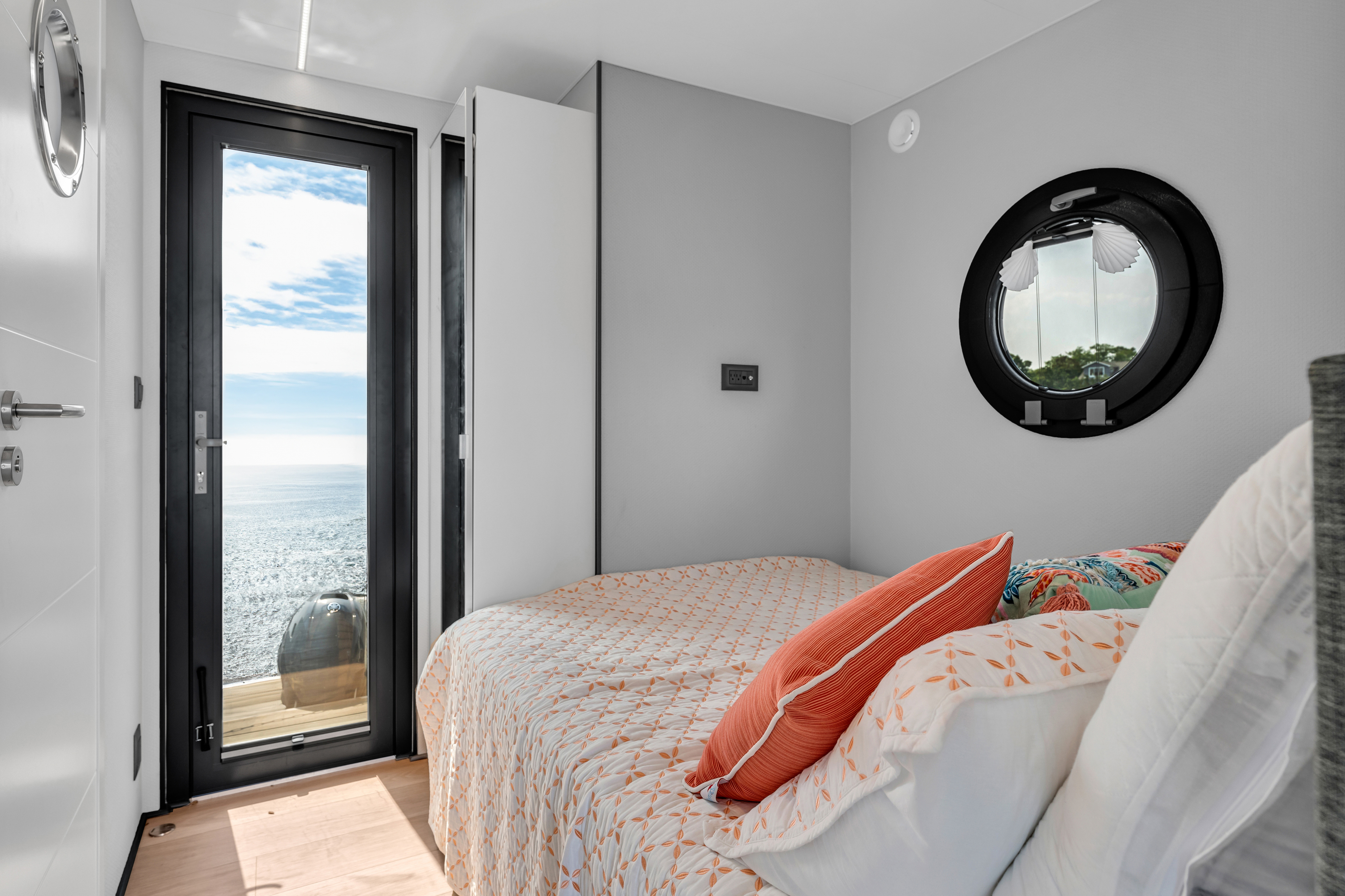 A modern bedroom with a bed, round mirror, and a door leading to a balcony.