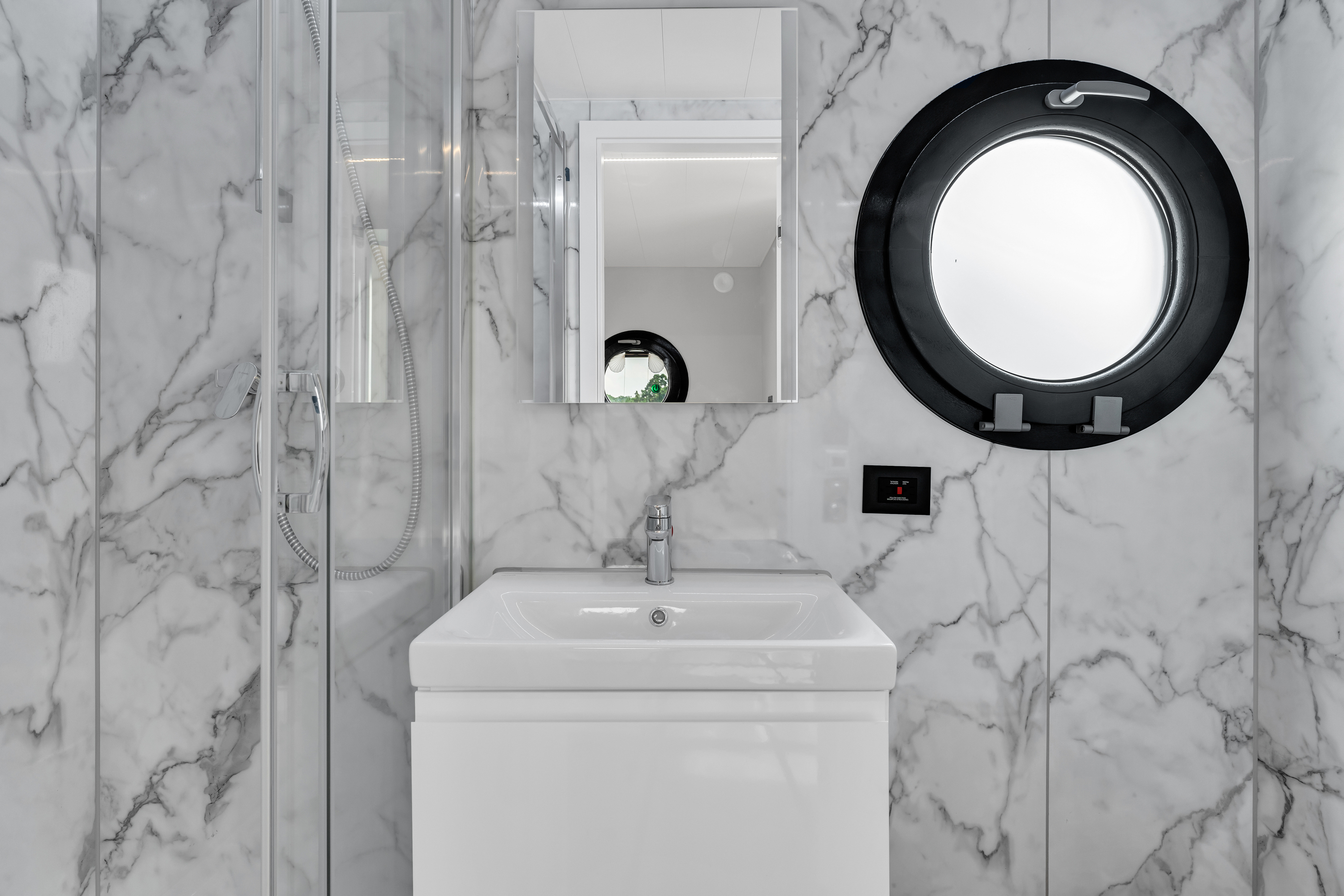 Modern bathroom with marble walls, a sink, mirror, and round light fixture.