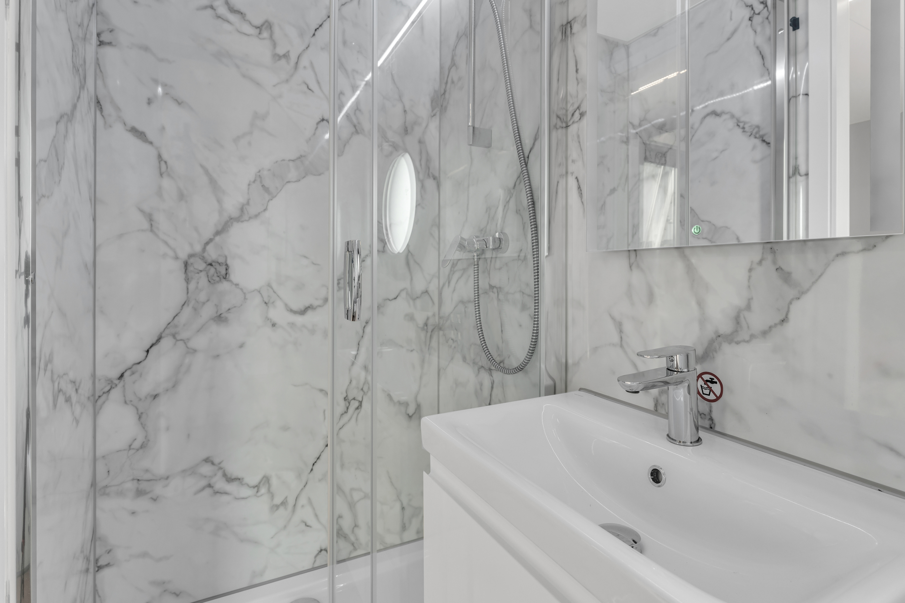 Modern bathroom with marble walls, glass shower, and white sink.